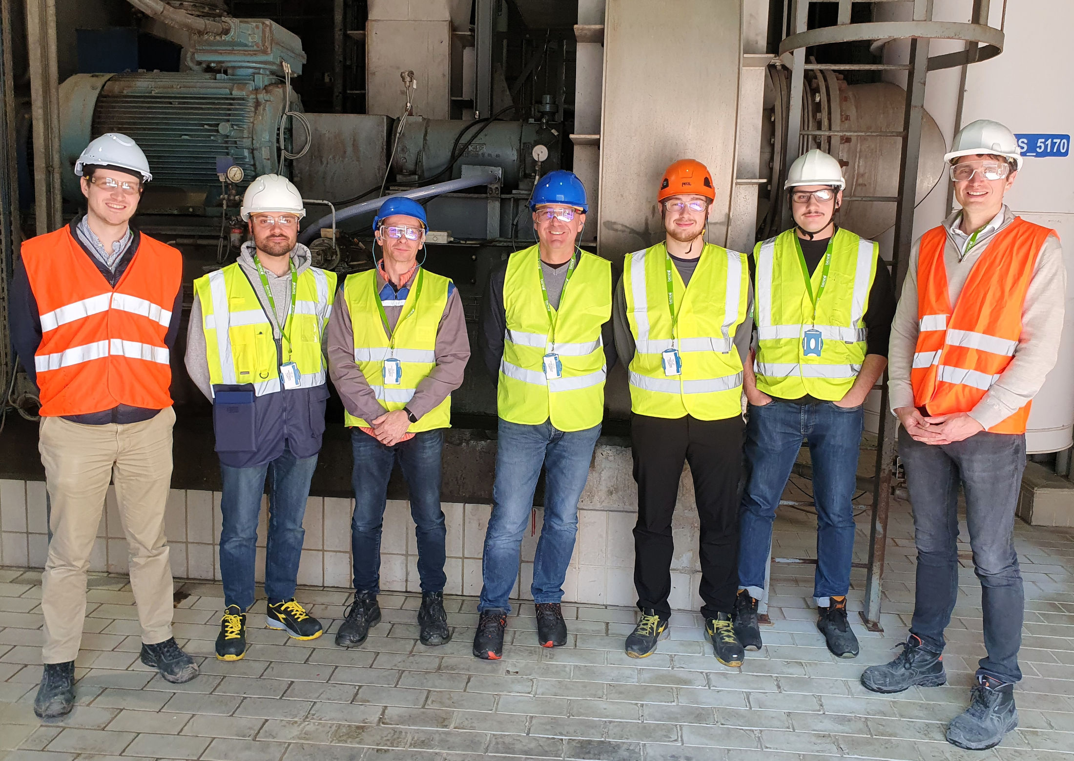 Équipe en visite terrain devant une installation industrielle avec équipements de procédé.